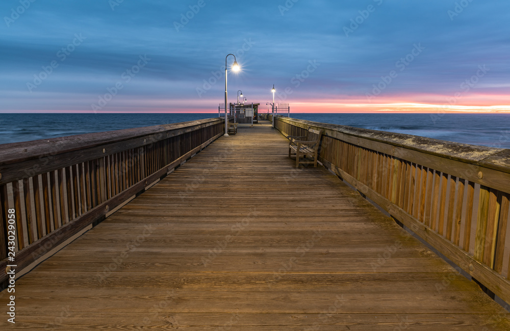 Sunrise from the Sandbridge Fishing Pier on Little Island Park in Virginia Beach.  The wood of the pier is lit by early morning sun rising in the clouds, creating pink and purple light.