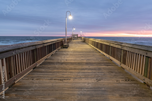 Sunrise from the Sandbridge Fishing Pier on Little Island Park in Virginia Beach.  The wood of the pier is lit by early morning sun rising in the clouds  creating pink and purple light.