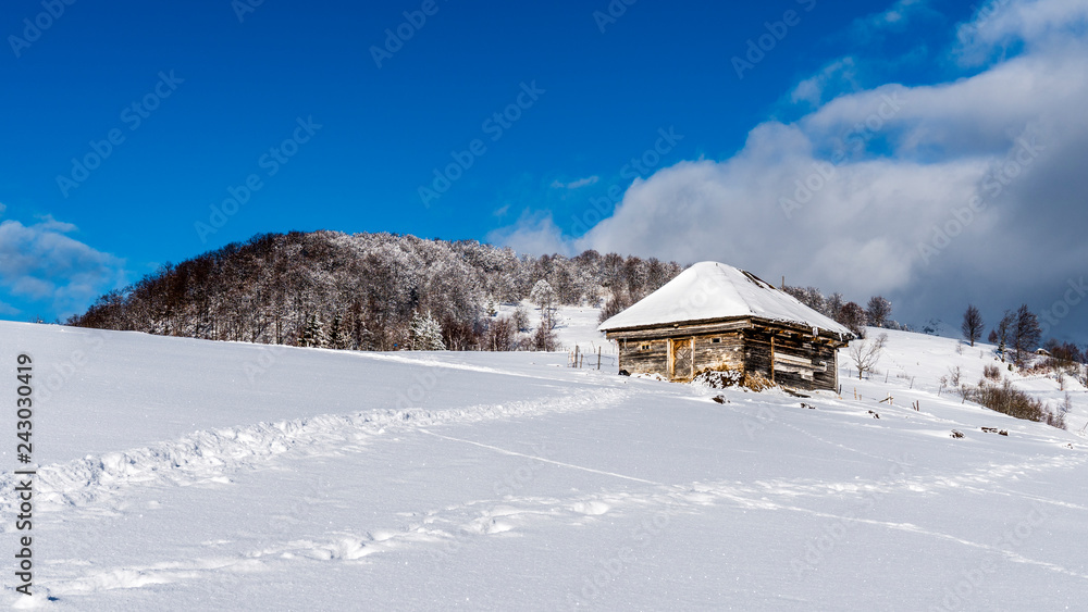 Mountain lodge in the picturesque Romania`s country side on a cold winter morning. Pristine clear ski  and snowy mountain peaks in the background. Piatra Craiului National Park.