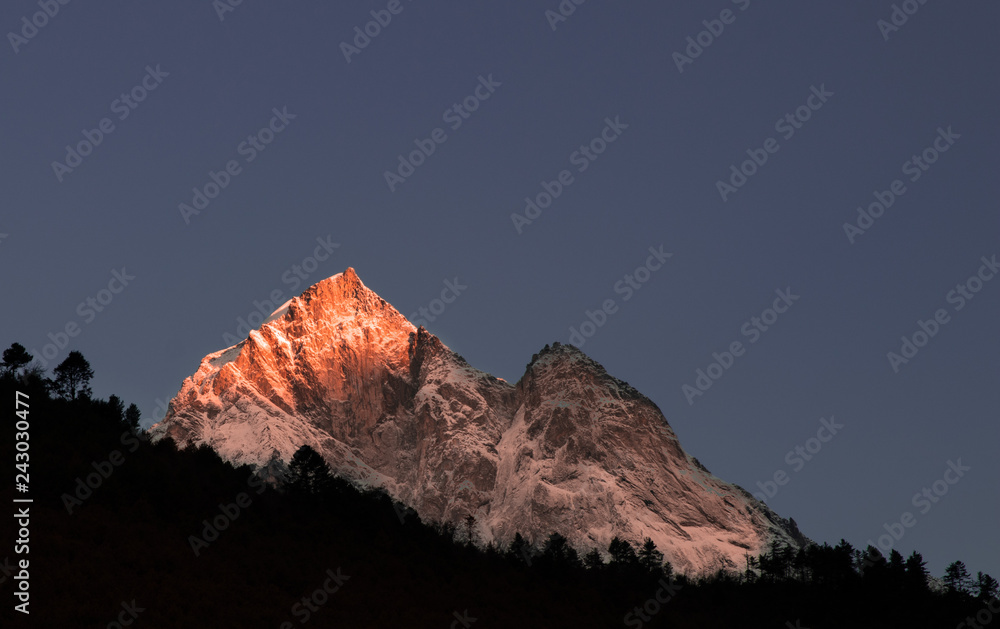 Sunrise over a mountain top with trees in the foreground. Photographed during an early morning walking the Everest Base Camp Trek.