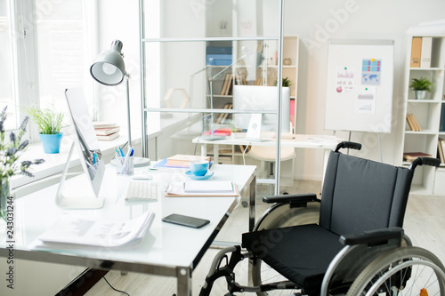 Modern office workplace with documents and computer monitor and wheelchair at the table