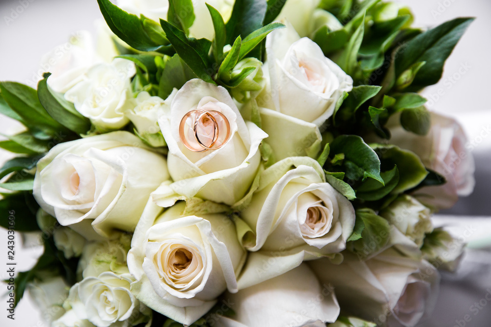 A pair of wedding rings on a bouquet of white roses, close up shot