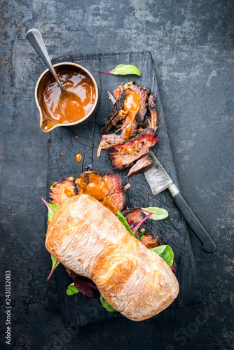 Traditional barbecue pulled pork piece of Bosten butt as sandwich with lettuce as top view on a black board