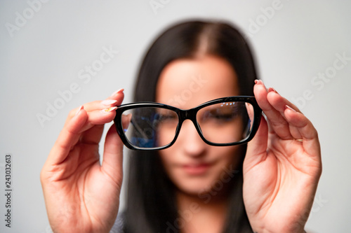 Smiling woman in blur background in optical store showing black classic frame for spectacles. New modern eyeglasses on the backgound of the woman. Macro shot