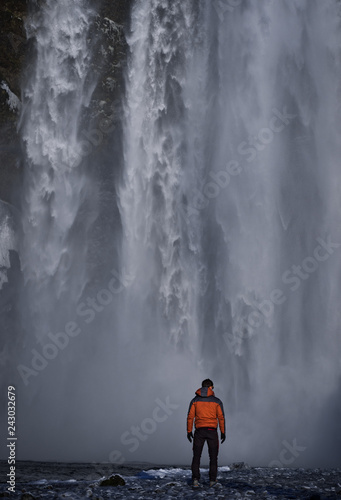 Person standing in front of Skogafoss waterfall in Iceland looking at the water.
