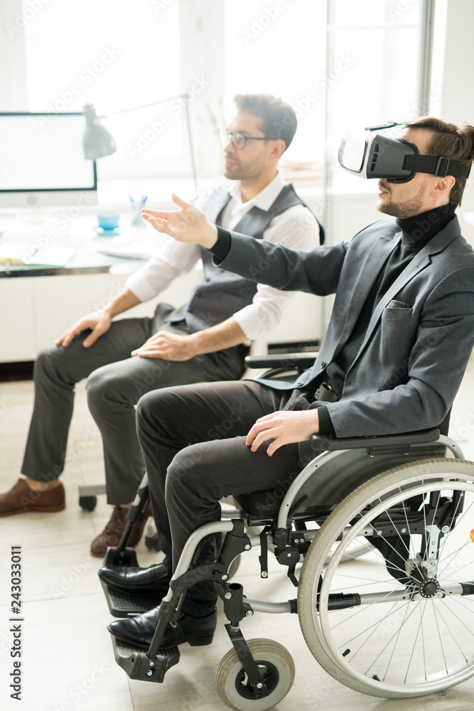 Young manager sitting in wheelchair and using VR goggles, he presenting modern gadgets to his business partner at office Young manager sitting in wheelchair and using VR goggles, he presenting modern gadgets to his business partner at office