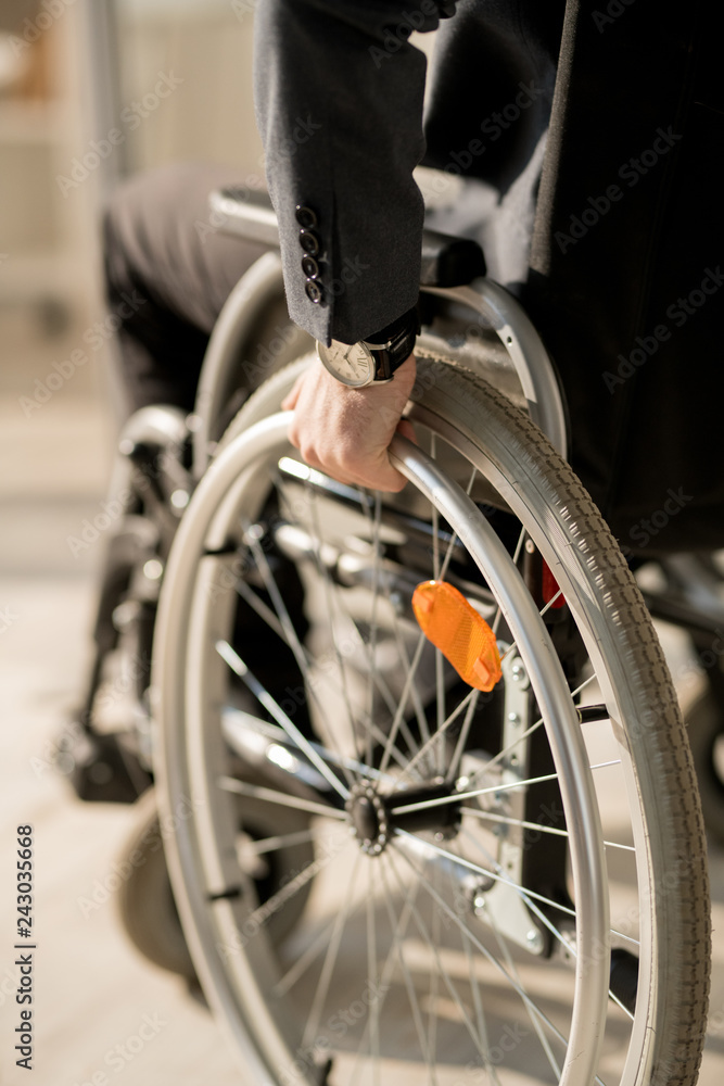 Close-up of handicapped businessman putting hand on the wheel while sitting in the wheelchair
