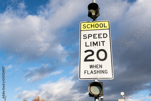Speed limit 20 when flashing sign near school. Cloudy sky in the background.