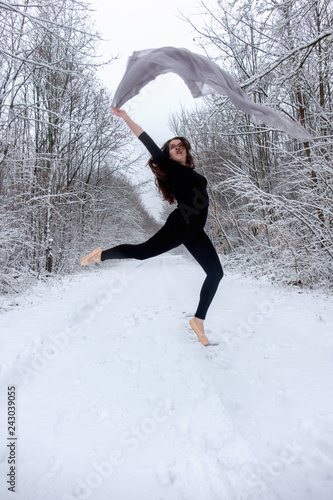 Junge schöne Frau Mädchen braunhaarig in schwarzem Ballett Anzug springt und tanzt Spitze im verschneiten Winter Wald 
