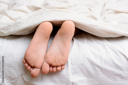 Little female child sleeps in bed and her bare feet are visible from under the blanket © Vitalii