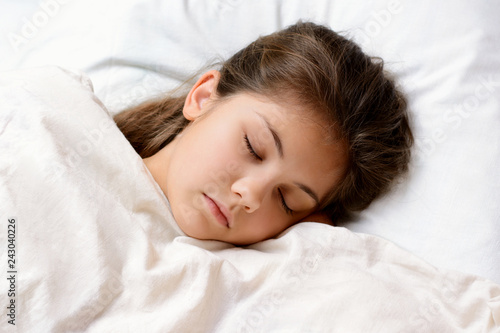 Beautiful young girl sleeping on comfortable warm bed after having games and playing with toys. Little girl has good sleep after hard day of studying. Concept of having good sleep at night