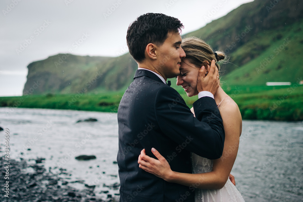 Portrait shot of young wedding couple  hugging under rain on background of mountain landscape