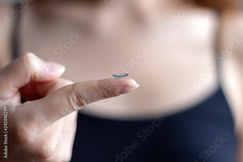 Girl holding contact lens in her fingers. Blurred background
