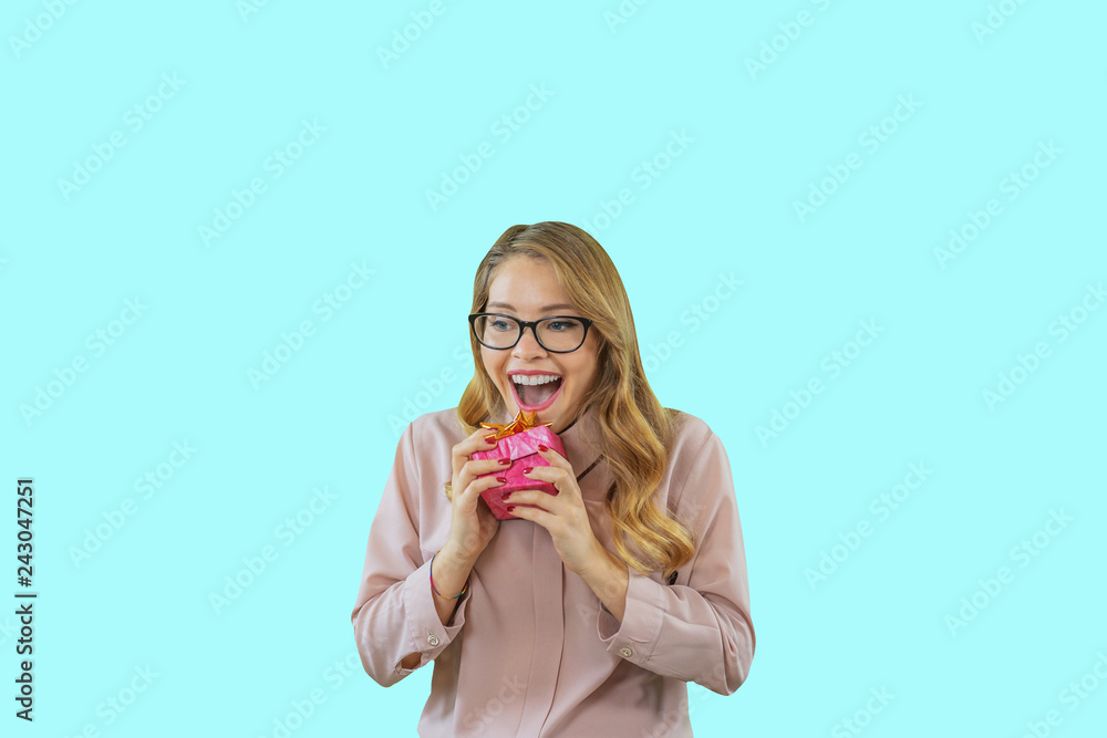 Portrait of a young beautiful blonde with glasses clutching a small box to herself smiles enthusiastically on an isolated background, New Year's holidays, birthday, marriage proposal Portrait of a young beautiful blonde with glasses clutching a small box to herself smiles enthusiastically on an isolated background, New Year's holidays, birthday, marriage proposal
