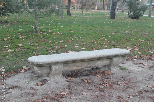 Gray stone bench, surrounded by vegetation, dry leaves and sand. photo taken with daylight