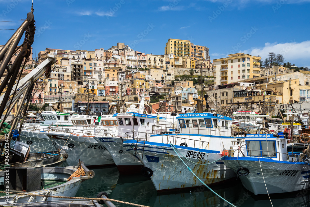 Fishing boats moored at Sciacca port with the colorful old town buildings on the background, Sicily, Agrigento province, Italy