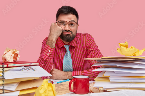 Canvas Print Lazy displeased fatigue male worker keeps fist on cheek, has sleepy look, dresse