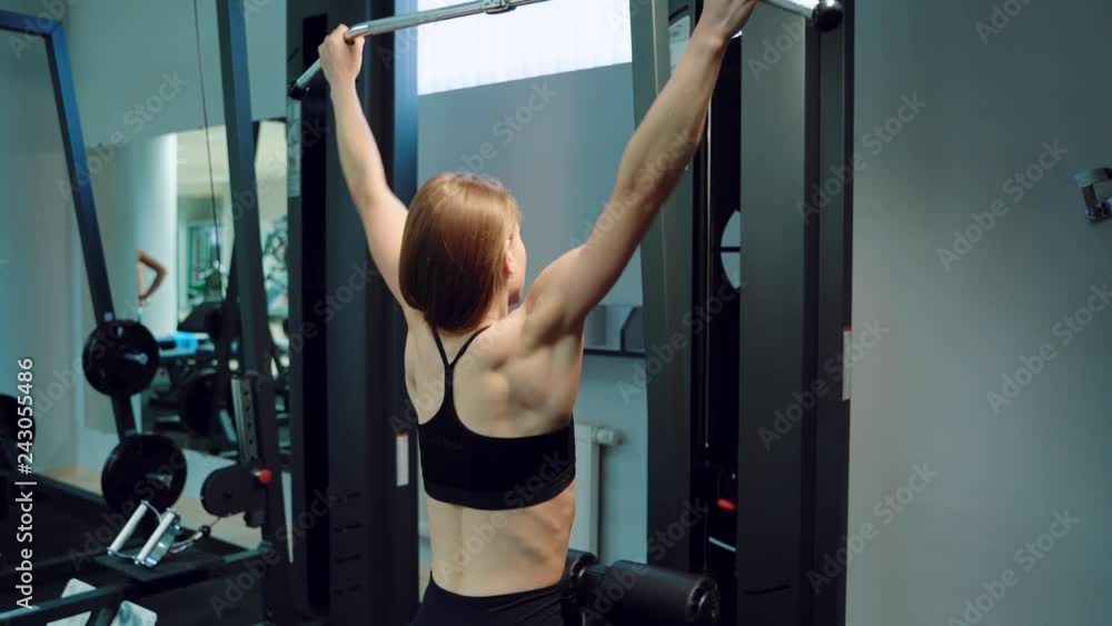 A strong woman in black top is doing vertical traction in the training in the fitness club. Close-up A strong woman in black top is doing vertical traction in the training in the fitness club. Close-up