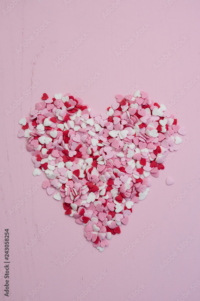 Top view flat lay with huge heart made of hundreds of small red, white and pink heart-shaped sweet sugar cupcake sprinkles as symbol for romantic love on wooden background for Valentine's Day card