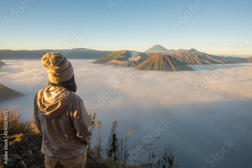 Back view of Asian women standing on the hill and looking to the beautiful sunrise and sea of fog over Bromo Tengger Semeru National Park in East Java, Indonesia.