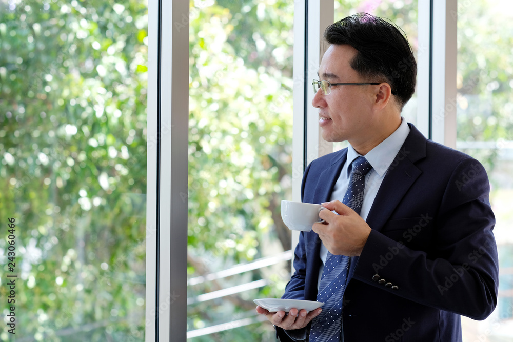 Asian Businessman holding coffe cup standing by windows, inside eco office building background, businessperson, office lifestyle Asian Businessman holding coffe cup standing by windows, inside eco office building background, businessperson, office lifestyle