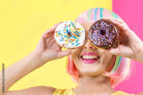 Beautiful woman in a colorful wig with doughnuts on a split yellow and pink background