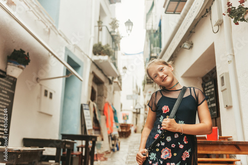 Funny little girl traveler walking on the streets of Valencia, wearing cross back. Travel with kids, family vacation on south of Spain, image taken in Peniscola