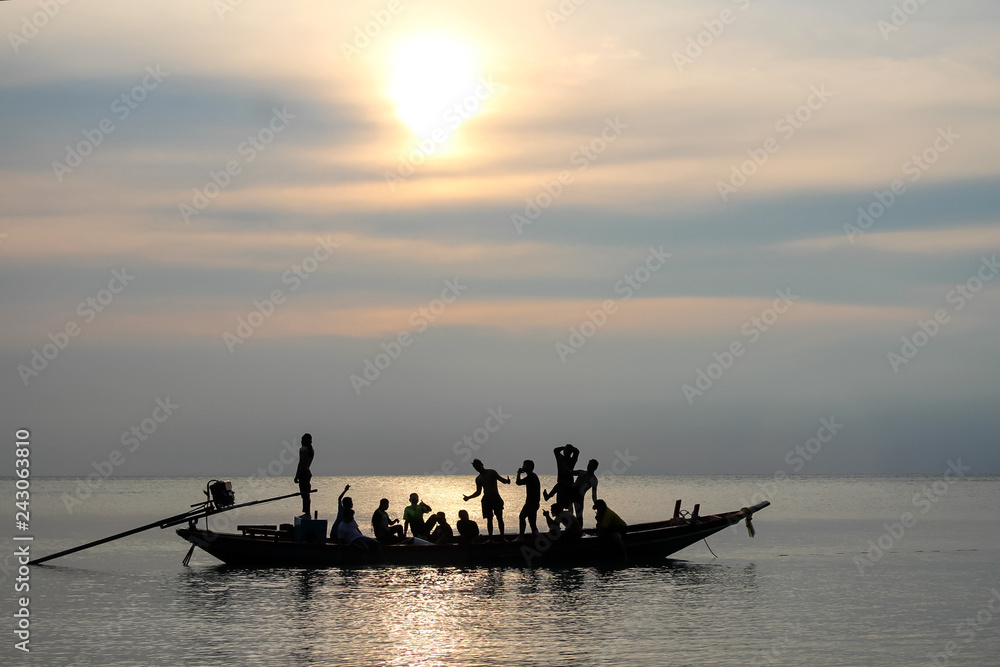 Silhouettes of people having fun on a long tail boat with sunset sky