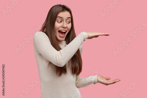 Happy overemotive young woman shows big size of recieved present, shares posi...