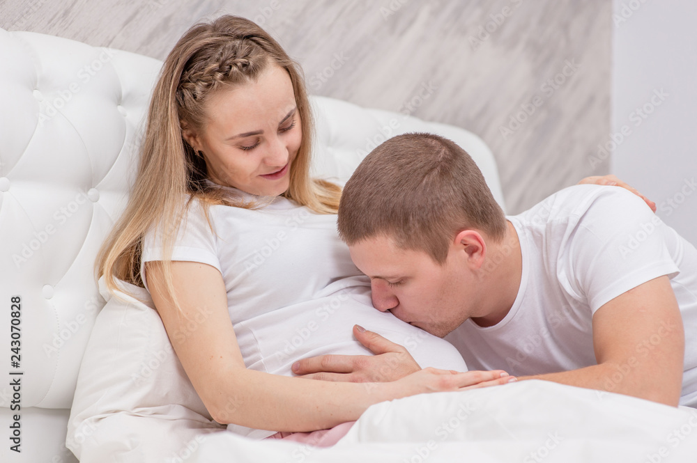 Fototapeta premium Husband kisses to the belly of his pregnant wife on the bed