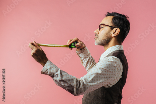 Картината върху платно Portrait of a tailor looking down at fabric measure, isolated on pink studio bac