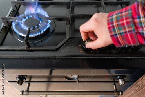 focus on fire. A man lighting the gas-stove with by means of automatic electric ignition. Modern gas burner and hob on a kitchen range. Dark black color and wooden Small kitchen in a modern apartment