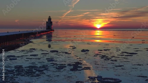 Iconic Lighthouse stands alone in frozen Lake Michigan harbor, Winter dawn, dynamic aerial view. photo