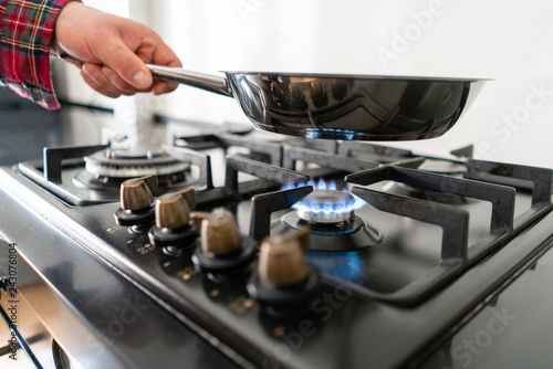 A man cooks in a frying pan, puts it on the stove. Modern gas burner and hob on a kitchen range. Dark black color and wooden Small kitchen in a modern apartment
