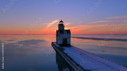 Iconic Lighthouse stands alone in frozen Lake Michigan harbor, Winter dawn, dynamic aerial view with dolly zoom effect. photo