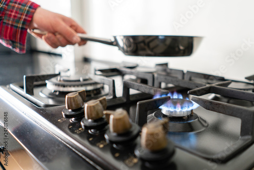 A man lighting the gas-stove with by means of automatic electric ignition. Modern gas burner and hob on a kitchen range. Dark black color and wooden Small kitchen in a modern apartment