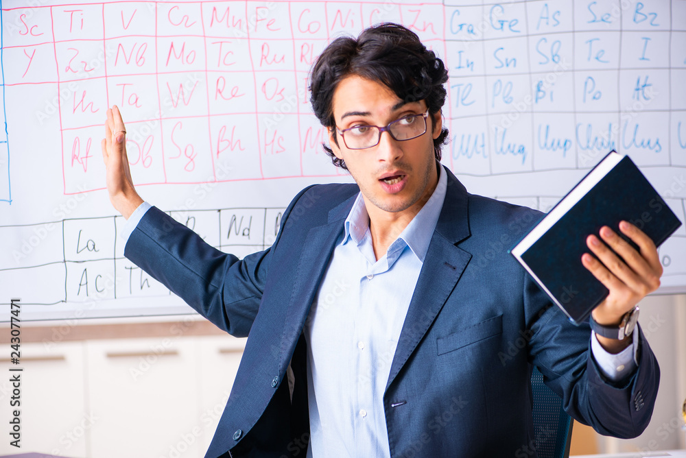 Young male chemistry teacher in front of periodic table Young male chemistry teacher in front of periodic table