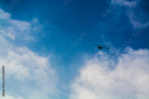 The blue sky with white clouds in the warm summer. Flight of the helicopter highly over the head.