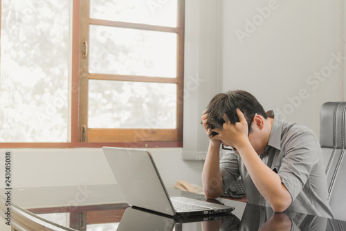 Businessman having stress with laptop computer working in the office,Exhausted asian man touching his head, he is having a bad headache, stress and overwork concept.