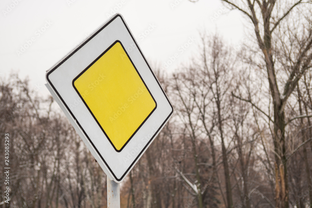 Main road sign mounted on metal pole on the background of trees. Priority road sign on the background of trees Main road sign mounted on metal pole on the background of trees. Priority road sign on the background of trees