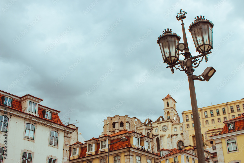 Street lamp against cloudy sky and historical center of Lisbon, Portugal. Lisbon landmark. Ancient architecture in Europe. Travel concept. Traditional medieval buildings. Old street lantern and houses