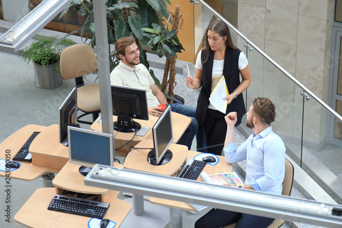 Top view of young modern colleagues in smart casual wear working together while spending time in the office. photo