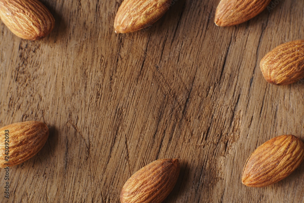 Almond nut in wooden bowl on wooden table with green leaf background Almond nut in wooden bowl on wooden table with green leaf background