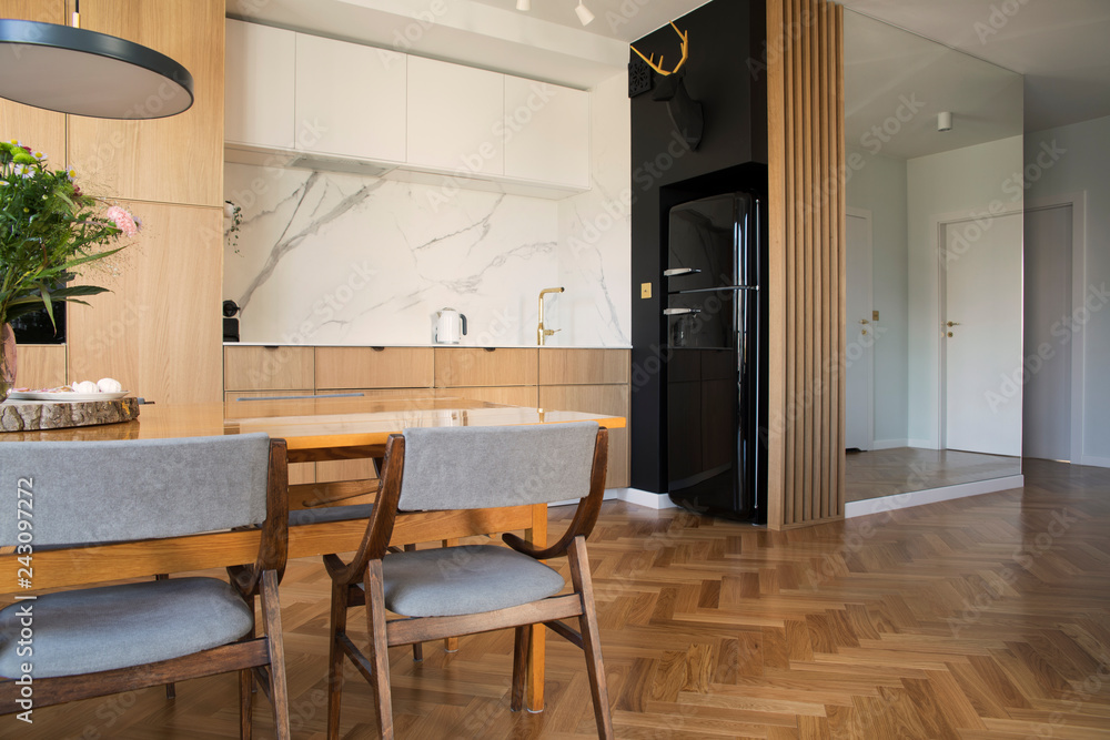 Stylish and cozy scandinavian dining and kitchen interior with family table, chairs and lamp. White marble walls , big mirror ont wall and brown wooden parquet. Stylish and cozy scandinavian dining and kitchen interior with family table, chairs and lamp. White marble walls , big mirror ont wall and brown wooden parquet.