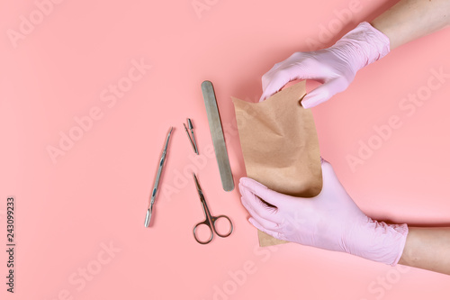 packing a manicure tool in kraft packages before sterilizing in a dry oven. Manicure tool in the hands of the master isolated on pink background. the concept of personal protective equipment © Надія Коваль