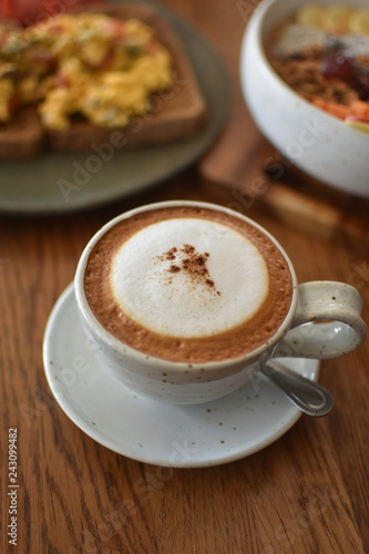 At stylish café in Thailand.Tasty cappuccino, with a hint of cinnamon in the middle of milk foam, looking from the side angle with delicious egg toast and fruits bowl in the background.Portrait mode.