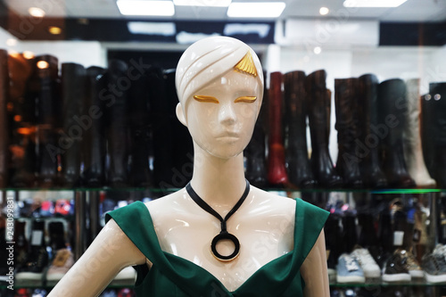 Female mannequin in green dress with gold hair and eyelashes with a big black neckless