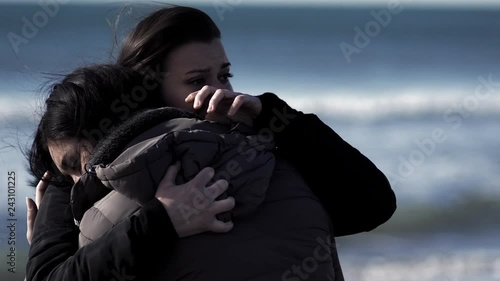 Two sister hugging and crying in front of the sea in winter super slow motion closeup