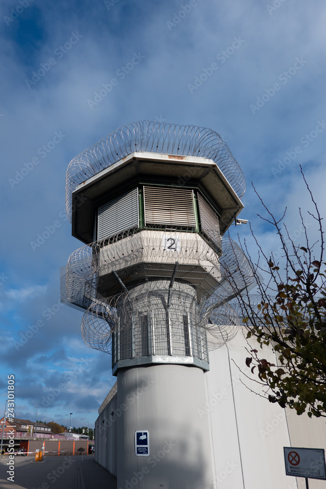 Watchtower of a correctional facility of a prison with a balustrade and two rows of barbed wire rolls in front of a dramatic sky