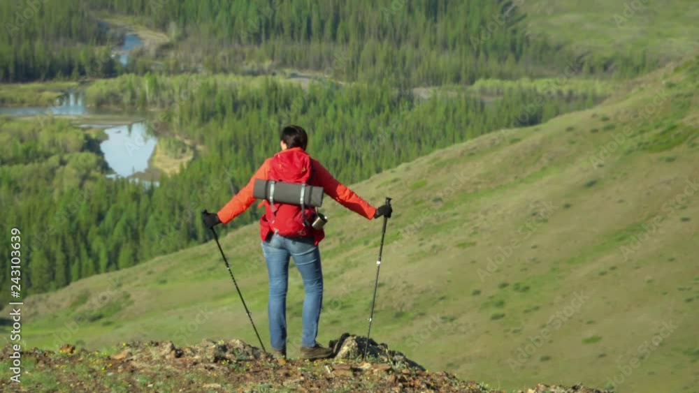 The woman the traveler with a red backpack rises by the mountain, looks at snow mountains. The woman the traveler with a red backpack rises by the mountain, looks at snow mountains.